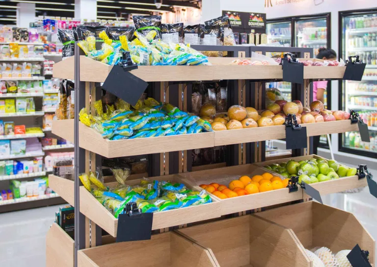 Supermarkt mit hohen Regalen, im Vordergrund steht ein Obst- und Gemüseregal.