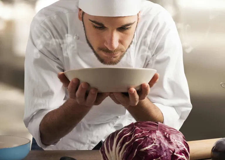 Ein Koch hält bedächtig einen Teller mit beiden Händen fest und atmet den Duft des frisch gekochten Essens ein