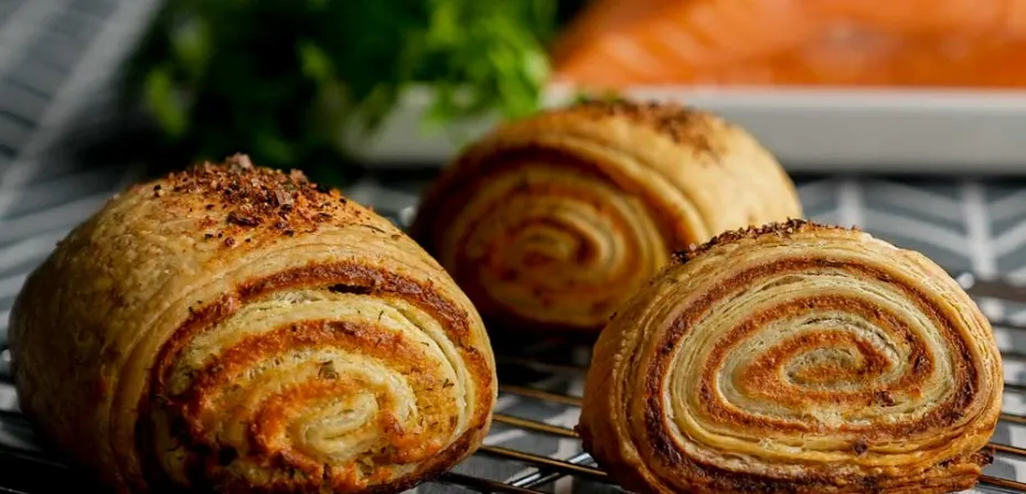 Knusprige Blätterteigrollen liegen auf einem Backblech.