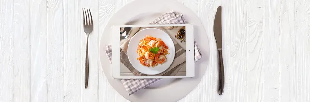 Ein Tablet liegt auf einem Teller. Auf dem Tablet ist ein Bild von einem Garnelengericht geöffnet.