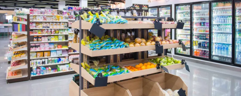 Supermarkt mit hohen Regalen, im Vordergrund steht ein Obst- und Gemüseregal.